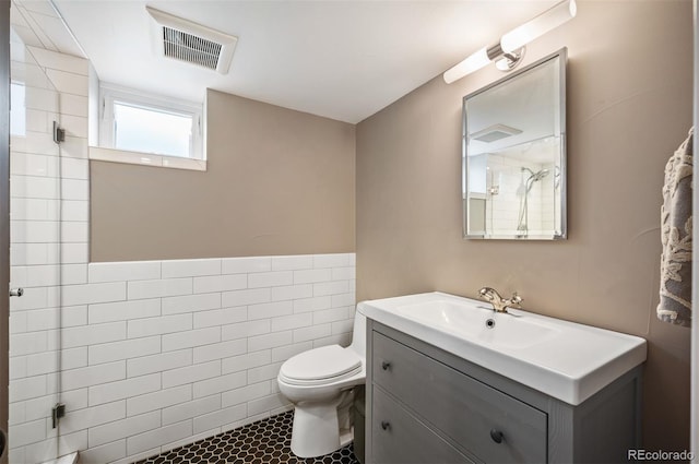 full bathroom with toilet, tiled shower, vanity, tile walls, and tile patterned floors