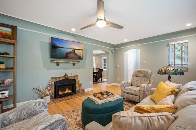 living room with arched walkways, wood finished floors, ceiling fan, recessed lighting, and a fireplace with flush hearth