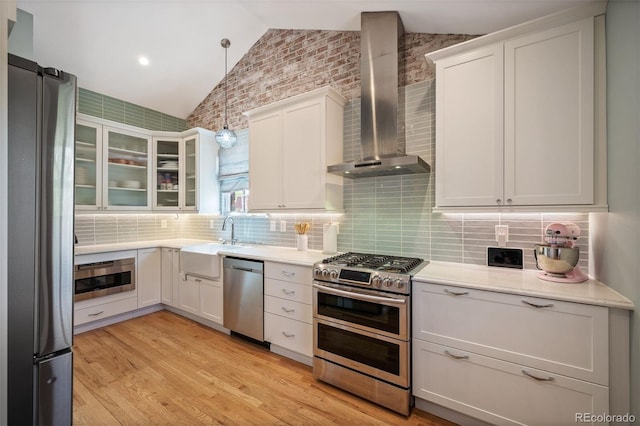 kitchen with stainless steel appliances, wall chimney exhaust hood, lofted ceiling, a sink, and light wood-style floors