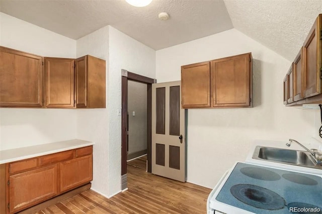 kitchen with stove, sink, vaulted ceiling, light wood-type flooring, and a textured ceiling