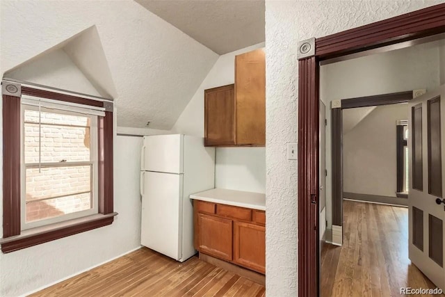 kitchen featuring a textured ceiling, white fridge, lofted ceiling, and light wood-type flooring