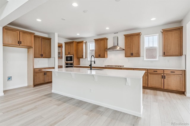 kitchen featuring a center island with sink, wall chimney range hood, sink, appliances with stainless steel finishes, and a kitchen bar