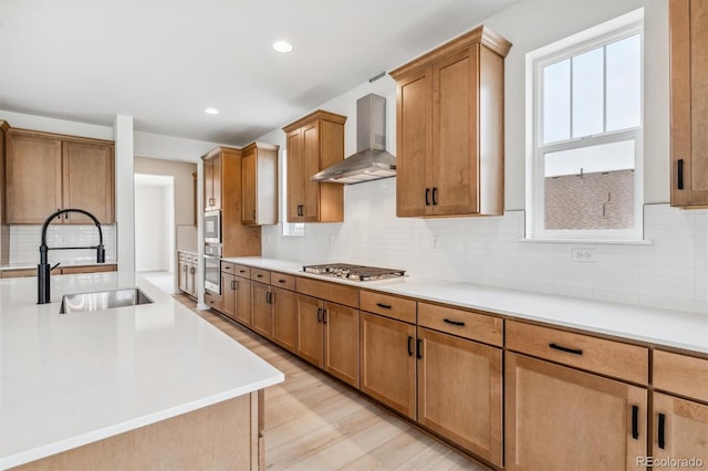 kitchen with backsplash, wall chimney range hood, sink, light hardwood / wood-style flooring, and stainless steel gas cooktop