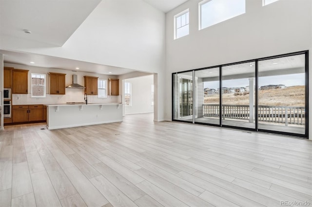 unfurnished living room featuring plenty of natural light, a towering ceiling, and light hardwood / wood-style floors