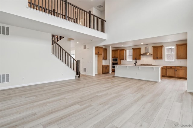 unfurnished living room featuring light wood-type flooring, a towering ceiling, and sink