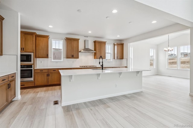 kitchen with a breakfast bar, a kitchen island with sink, sink, wall chimney exhaust hood, and appliances with stainless steel finishes