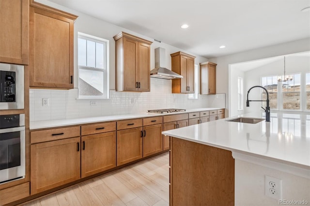 kitchen with sink, wall chimney exhaust hood, an inviting chandelier, light hardwood / wood-style floors, and appliances with stainless steel finishes