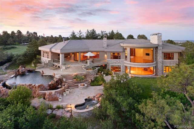 606 Cliffgate Ln, Castle Rock, CO 80108 - back of property at dusk featuring a patio, an outdoor fire pit, a chimney, and stone siding