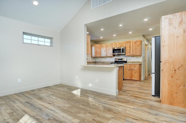 kitchen with kitchen peninsula, light hardwood / wood-style flooring, stainless steel appliances, a breakfast bar, and vaulted ceiling