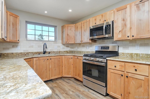 kitchen with appliances with stainless steel finishes, backsplash, sink, and light hardwood / wood-style flooring