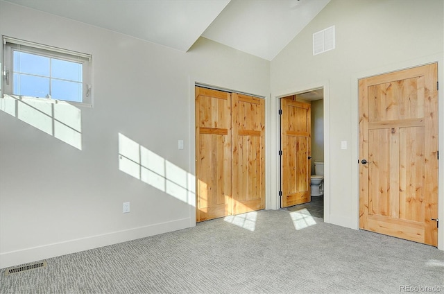 unfurnished bedroom featuring light carpet, a closet, ensuite bathroom, and high vaulted ceiling