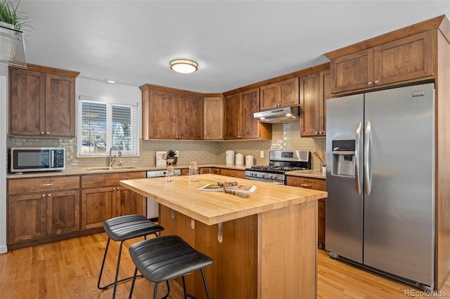 kitchen with sink, wooden counters, a breakfast bar, a kitchen island, and appliances with stainless steel finishes