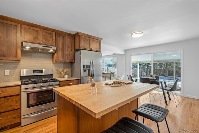 kitchen with appliances with stainless steel finishes, backsplash, light hardwood / wood-style flooring, a center island, and a breakfast bar area