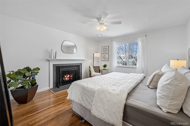 bedroom featuring a fireplace, hardwood / wood-style flooring, and ceiling fan