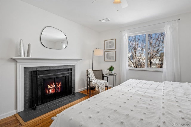 bedroom featuring ceiling fan, dark wood-type flooring, and a tiled fireplace