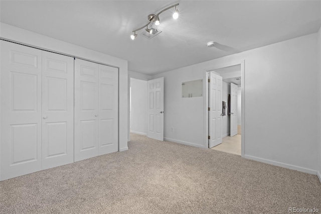 unfurnished bedroom with rail lighting, light colored carpet, and a closet