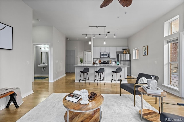 living room with light wood finished floors, ceiling fan, baseboards, and rail lighting