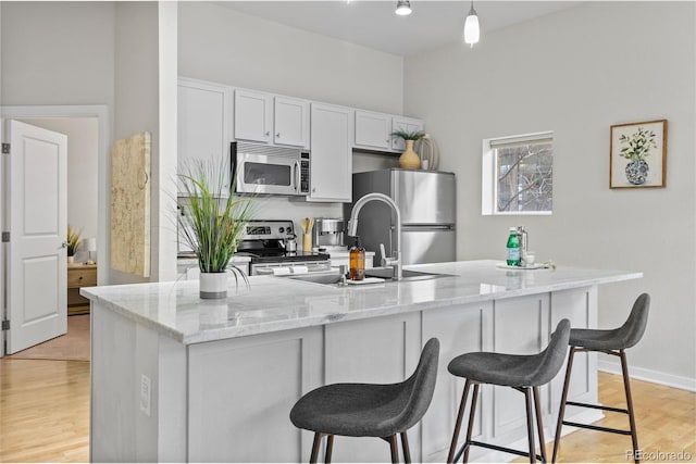 kitchen with light stone counters, a breakfast bar area, stainless steel appliances, light wood-style floors, and a center island with sink