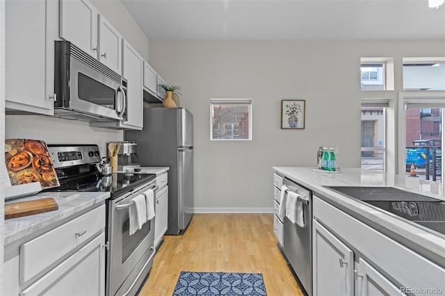 kitchen with appliances with stainless steel finishes, light wood-type flooring, white cabinets, and baseboards