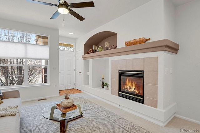 living area featuring a tile fireplace, carpet flooring, a ceiling fan, built in features, and baseboards