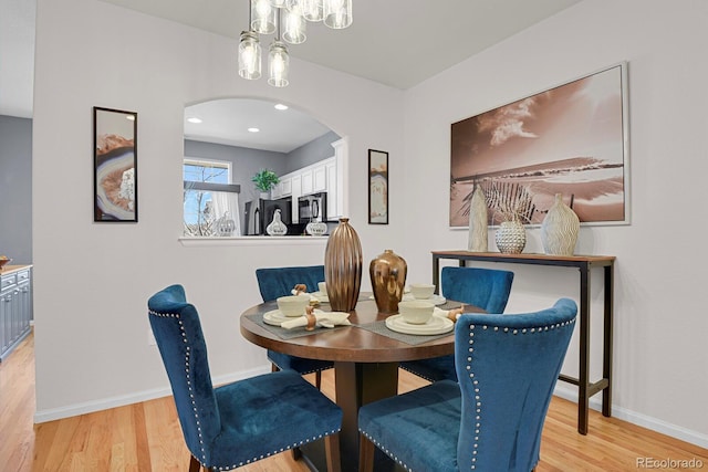 dining space with arched walkways, baseboards, and light wood finished floors