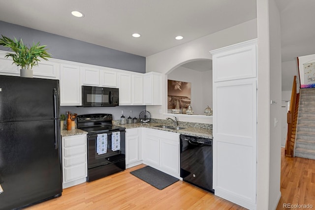 kitchen with black appliances, light wood-type flooring, a sink, and white cabinets