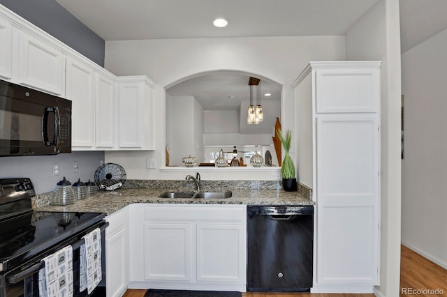 kitchen with black appliances, stone countertops, white cabinetry, and a sink