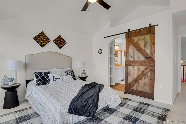 carpeted bedroom with a barn door, arched walkways, lofted ceiling, ceiling fan, and ensuite bathroom