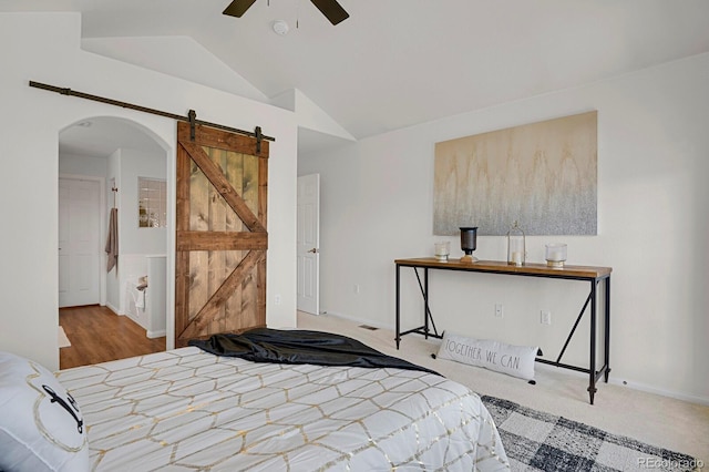 bedroom featuring lofted ceiling, arched walkways, a barn door, baseboards, and carpet