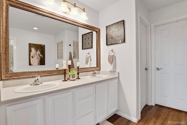 full bath featuring double vanity, a sink, baseboards, and wood finished floors