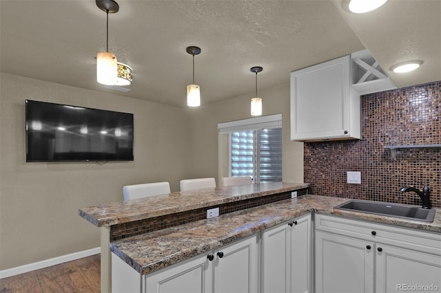 9455 Shinnecock Ct, Peyton, CO 80831 - kitchen with a peninsula, a sink, wood finished floors, white cabinets, and a textured ceiling