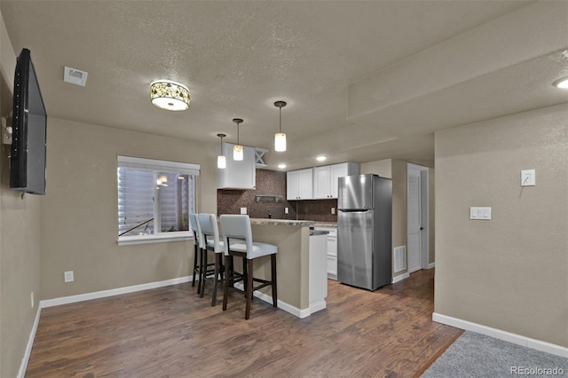 9455 Shinnecock Ct, Peyton, CO 80831 - kitchen with freestanding refrigerator, dark wood-style floors, white cabinets, a breakfast bar area, and a peninsula