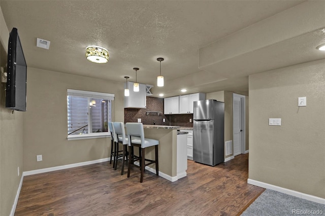 9455 Shinnecock Ct, Peyton, CO 80831 - kitchen featuring freestanding refrigerator, dark wood-type flooring, a peninsula, tasteful backsplash, and white cabinets