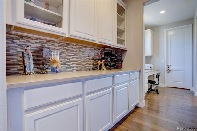 bar featuring built in desk, white cabinets, light wood-type flooring, and decorative backsplash