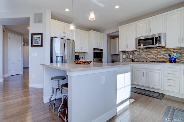 kitchen with white cabinetry, stainless steel appliances, decorative light fixtures, and a kitchen island