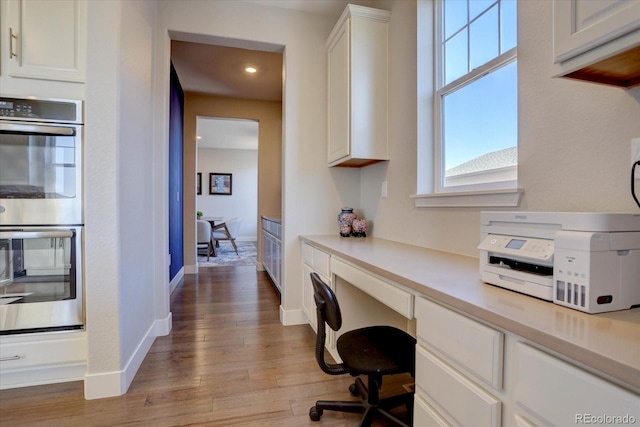 office space with built in desk and light hardwood / wood-style flooring