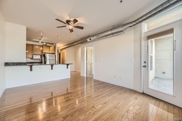 unfurnished living room featuring light wood-style flooring, a ceiling fan, and baseboards