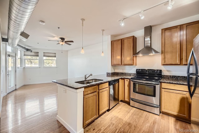 kitchen with stainless steel appliances, a sink, wall chimney exhaust hood, brown cabinets, and a peninsula