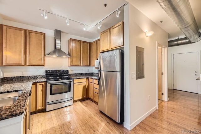 kitchen featuring stainless steel appliances, wall chimney range hood, electric panel, light wood-type flooring, and a sink