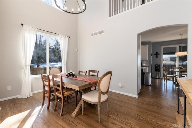 dining space with dark wood-type flooring, a chandelier, and a towering ceiling