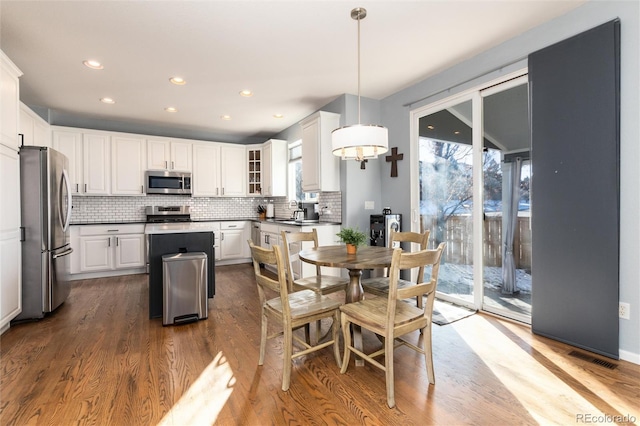 kitchen with white cabinetry, stainless steel appliances, tasteful backsplash, hanging light fixtures, and hardwood / wood-style flooring