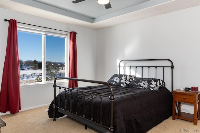 bedroom featuring ceiling fan, a tray ceiling, and light carpet