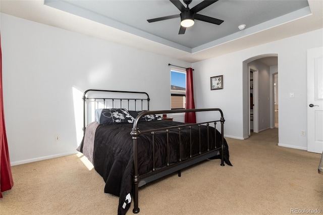 bedroom featuring ceiling fan, light colored carpet, and a raised ceiling