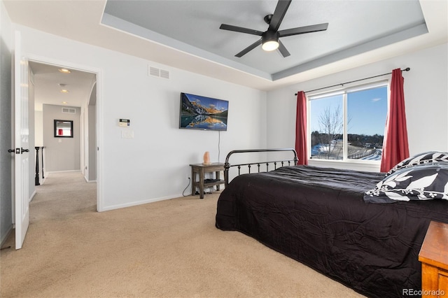 bedroom featuring a raised ceiling, light colored carpet, and ceiling fan