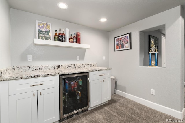 bar with light stone countertops, beverage cooler, white cabinetry, and carpet flooring