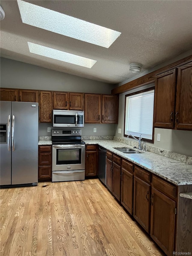 kitchen with lofted ceiling with skylight, sink, a textured ceiling, appliances with stainless steel finishes, and light stone counters