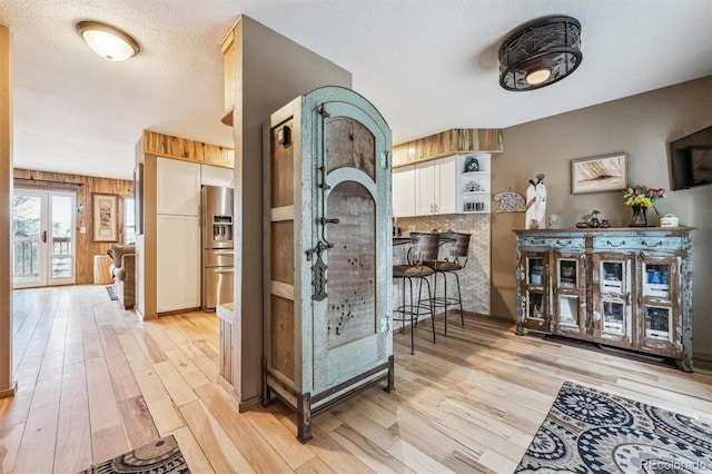 interior space with light wood-style floors, white cabinets, a textured ceiling, and stainless steel fridge with ice dispenser