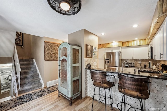 kitchen featuring visible vents, decorative backsplash, appliances with stainless steel finishes, light wood-type flooring, and a kitchen breakfast bar