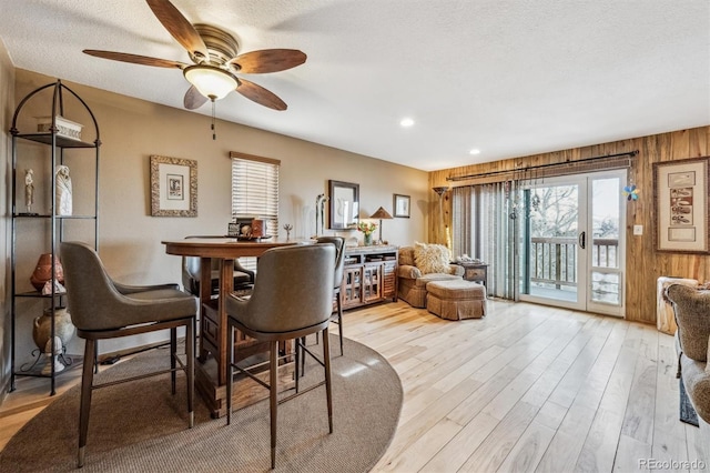 dining space with light wood-type flooring, wood walls, a textured ceiling, and ceiling fan