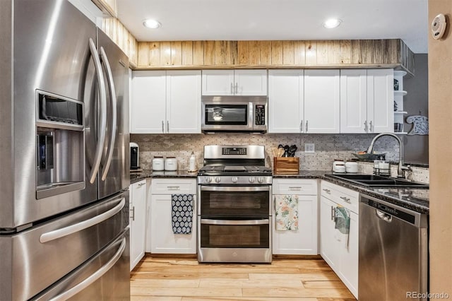 kitchen featuring a sink, appliances with stainless steel finishes, open shelves, light wood finished floors, and tasteful backsplash